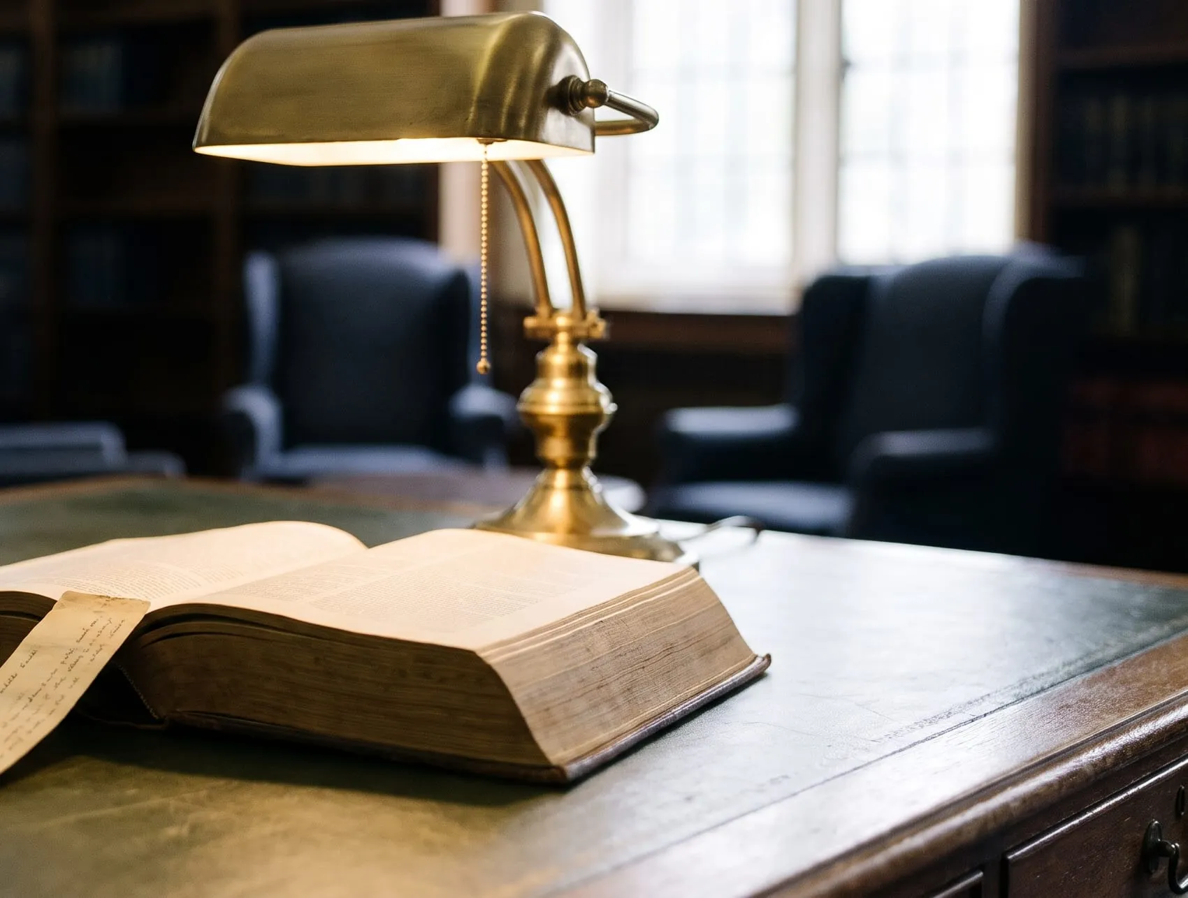 An open reference book with a ribbon marker, under a brass desk lamp.